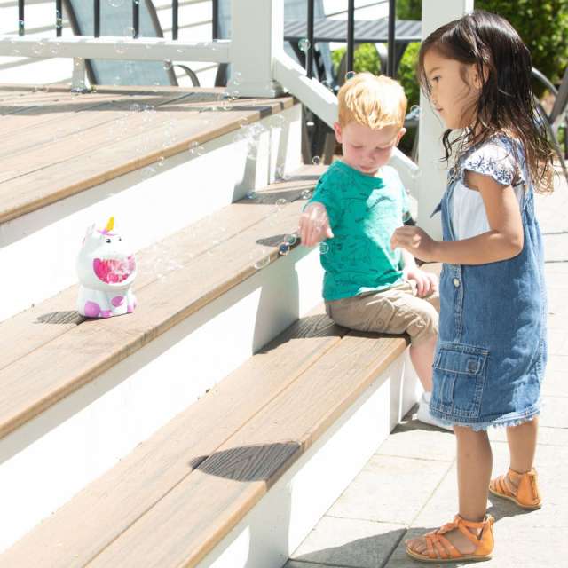 Young boy and girl playing on outdoor steps with a unicorn bubble machine blowing bubbles